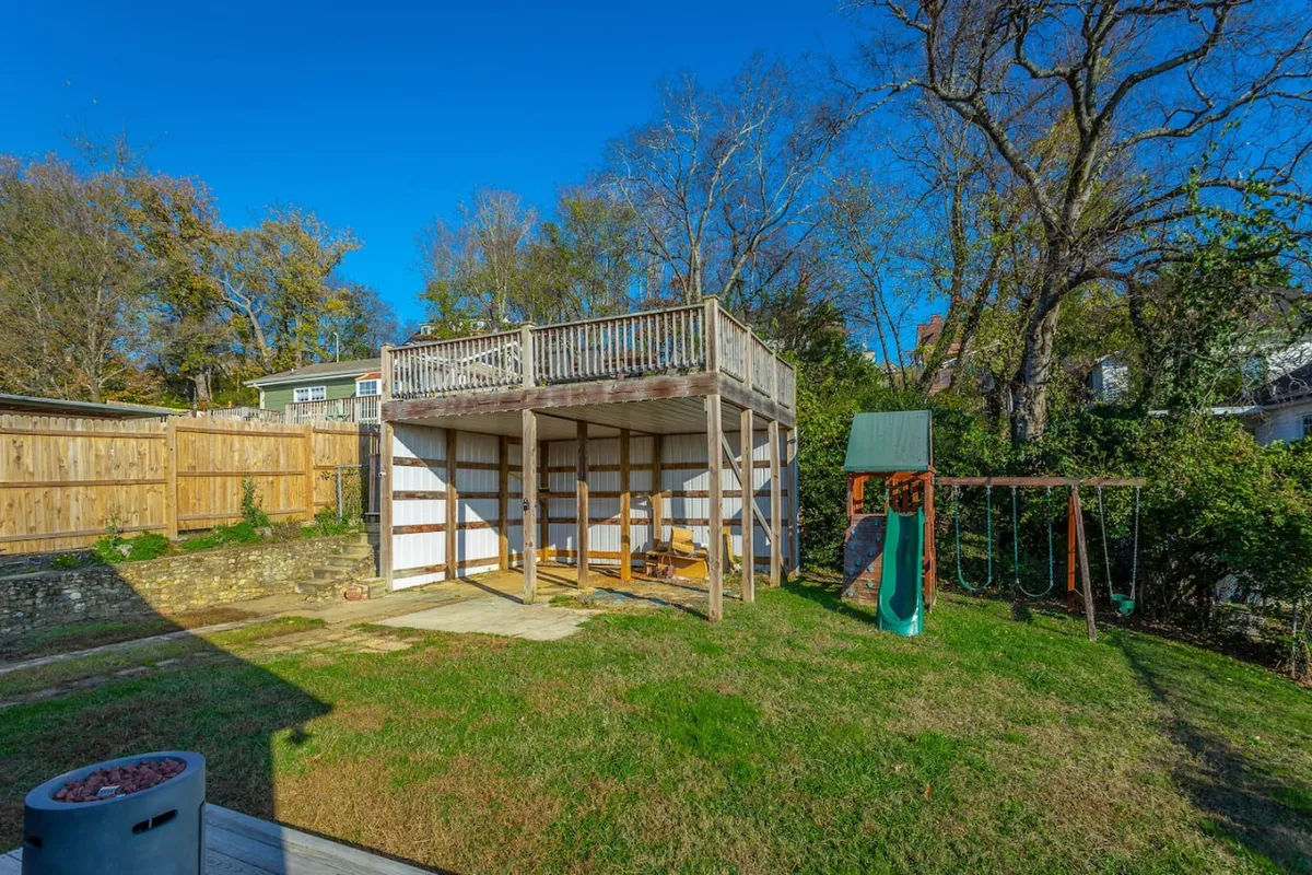 An exterior view featuring a raised deck, playground equipment, and a securely fenced yard. The scene is playful and family-friendly, with plenty of room for children to play and adults to relax or host gatherings.