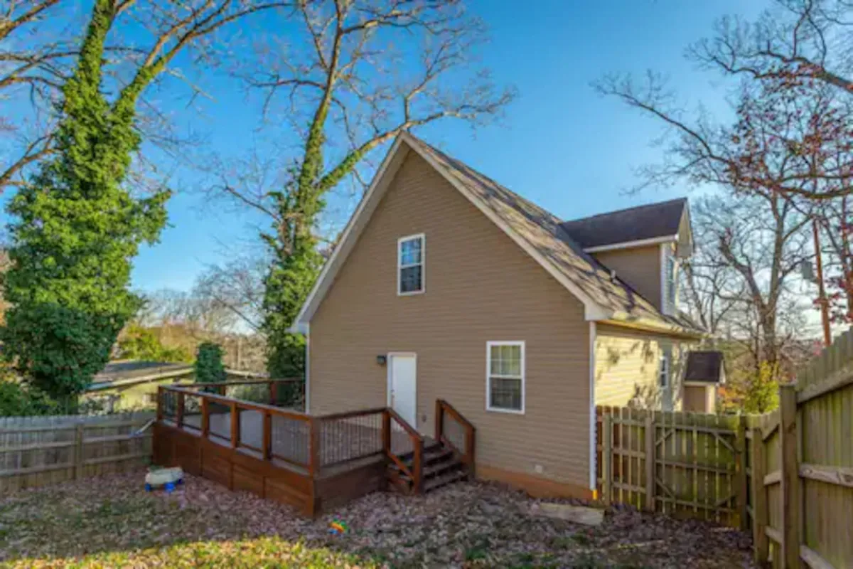 A backyard deck surrounded by a fence and lush trees. The open space is perfect for gatherings, barbecues, or relaxing after a day exploring the city.