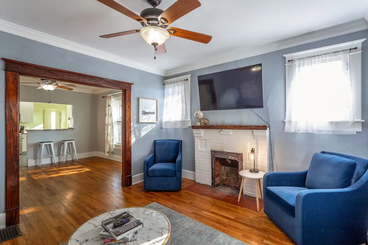 A cozy living room featuring blue chairs positioned around a modern fireplace and a TV, with a coffee table in the center. The room exudes warmth and comfort, ideal for smaller gatherings or relaxed downtime.