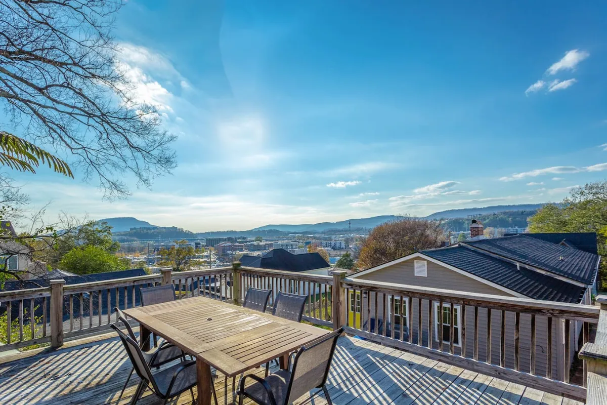 A spacious wooden deck with an outdoor dining table overlooks a sweeping city and mountain view. The setting invites large group meals, morning coffee, or sunset celebrations while taking in the scenic beauty surrounding Chattanooga.