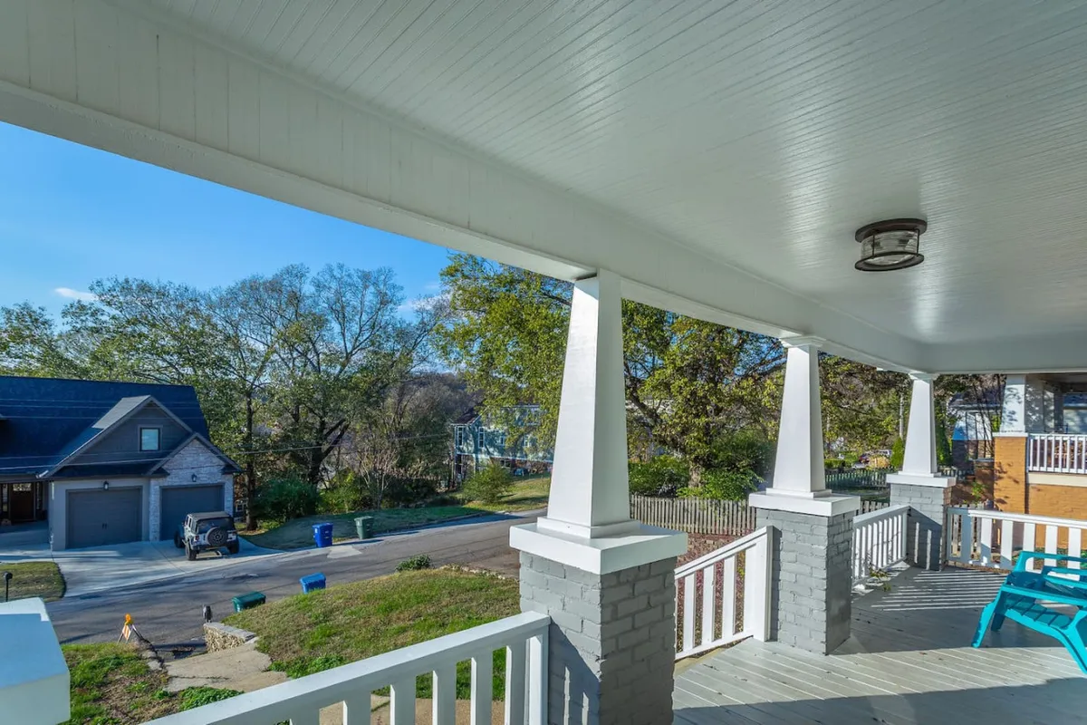 An inviting exterior view of a porch with blue chairs and a street scene in the background. The porch railing frames the space, creating a welcoming spot to relax and watch neighborhood activity.