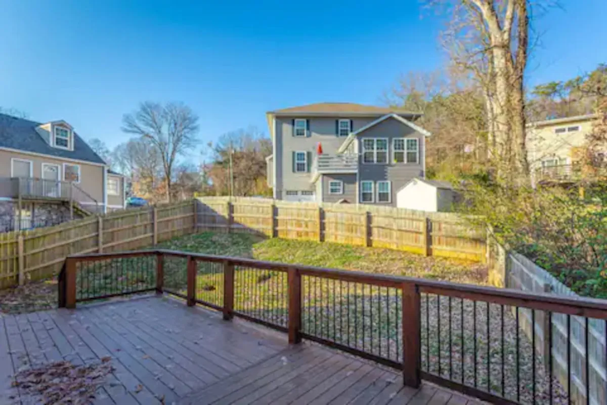 A welcoming deck and fenced backyard bordered by trees, offering space for barbecuing, gardening, or simply relaxing. Distant houses create a neighborhood feel, while the area is clearly designed for group activities.