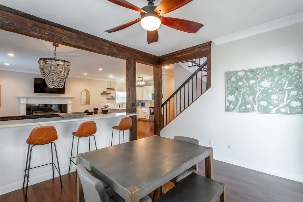 A spacious dining area featuring a large table surrounded by bar stools and illuminated by a stylish chandelier. The open layout and inviting décor are ideal for shared meals, festive celebrations, or quiet reflection.