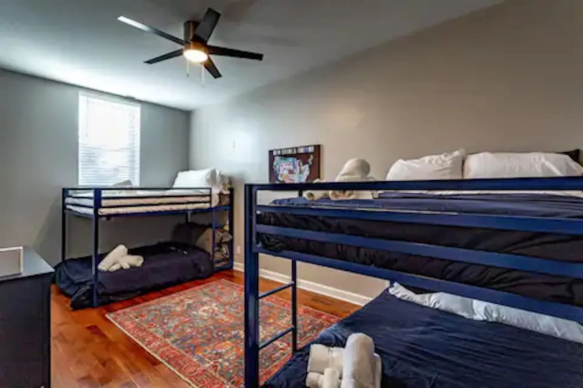 A playful and colorful bedroom designed for children, showcasing sturdy bunk beds, a vibrant area rug, and a ceiling fan. The cheerful design encourages bonding and memorable sleepovers for younger guests.