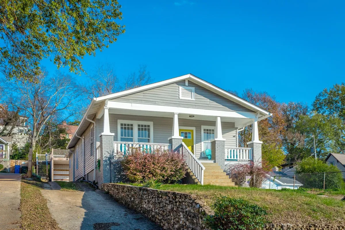 The image showcases the exterior of two welcoming downtown Chattanooga homes, featuring a charming front porch with a bright yellow door, surrounded by a beautifully landscaped garden. The inviting porch sets the scene for relaxation or gatherings, while the vibrant door and lush greenery create a cheerful, welcoming vibe.