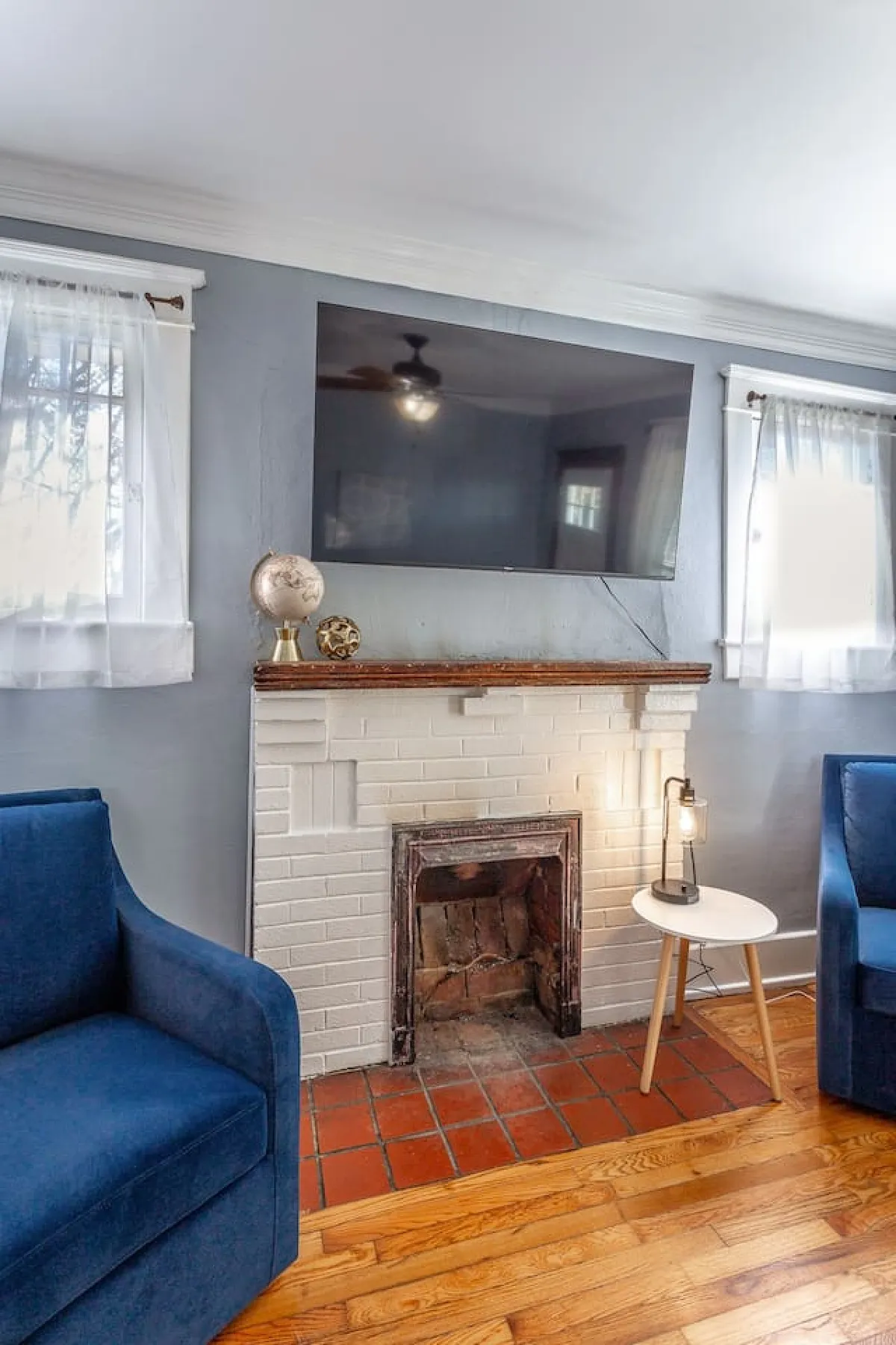 A stylish living room with blue armchairs, a fireplace, a TV, a side table, and a decorative globe. The space is designed for relaxation, socializing, and entertainment, with a layout that encourages conversation and connection.